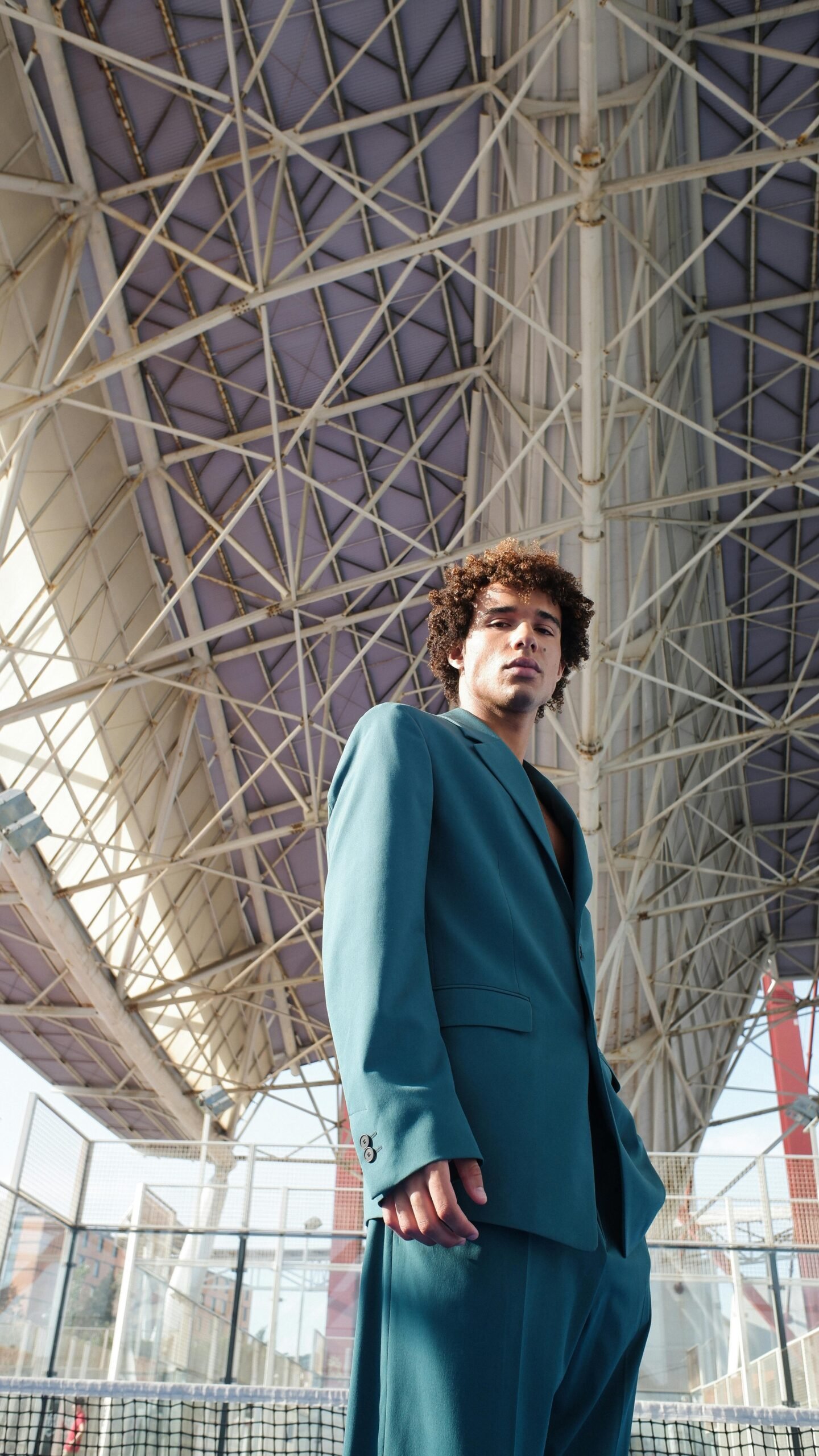 A man in a blue suit stands confidently beneath a modern architectural structure.